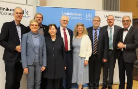 Gruppe Menschen steht vor Plakatwand und lächelt in die Kamera